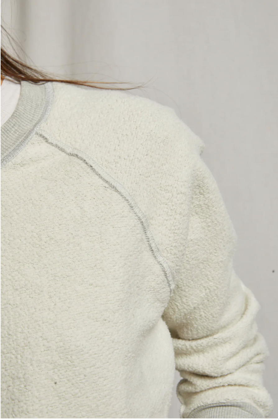 Close-up of a person wearing a Perfectwhitetee Ziggy Reverse Fleece LS Shrunken Crewneck Sweatshirt with visible texture and seams, emphasizing details in the fabric. The background is plain and neutral-colored, echoing the simplicity of a bungalow.