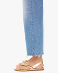 Side view of a person's lower leg wearing Mother's Maven Ankle Fray jeans and gold strappy sandals, standing against a white background.