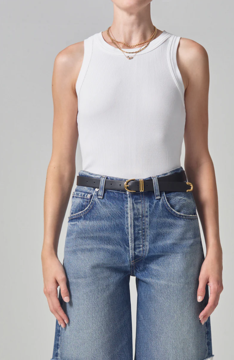 A person wearing a white ribbed racerback Isabel Rib Tank made of organic cotton and high-waisted blue jeans with a black belt, showcased from the waist to the neck. The focus is on casual fashion styling. (Brand Name: Citizens Of Humanity/AGOLDE)