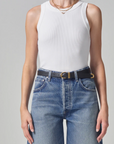 A person wearing a white ribbed racerback Isabel Rib Tank made of organic cotton and high-waisted blue jeans with a black belt, showcased from the waist to the neck. The focus is on casual fashion styling. (Brand Name: Citizens Of Humanity/AGOLDE)