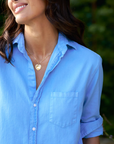 Close-up of a smiling woman wearing a Frank & Eileen Mary Classic Shirtdress and a heart-shaped pendant necklace, standing outdoors with greenery in the background in Scottsdale, Arizona.