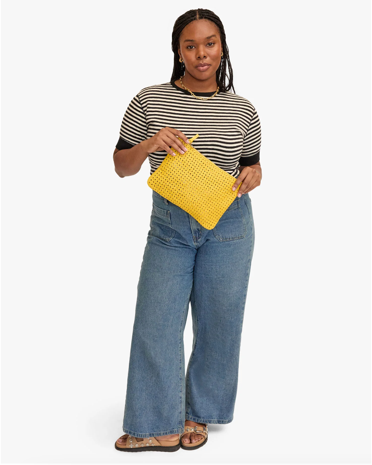 Woman in striped t-shirt and jeans holding a Clare Vivier Flat Clutch w/ Tabs, standing against a white background in Arizona style.