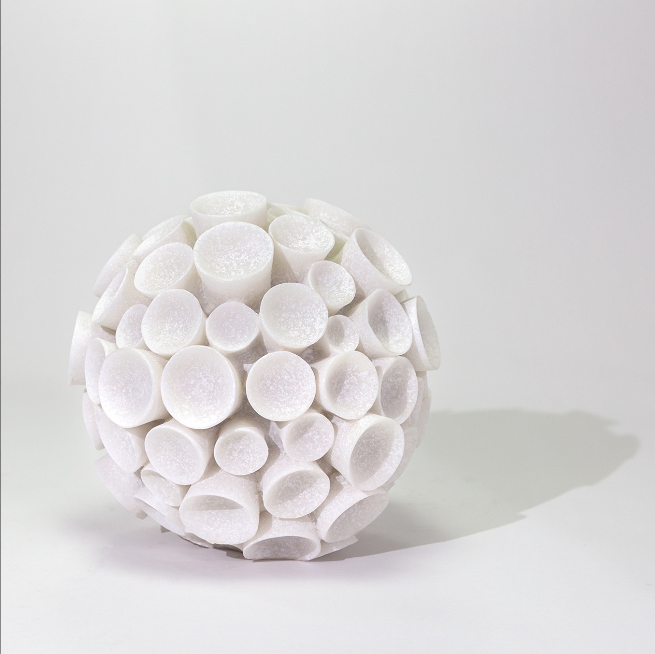 A spherical sculpture composed of numerous Lela coral statuary elements against a light grey background, casting a soft shadow in Scottsdale Arizona. (from The Import Collection)