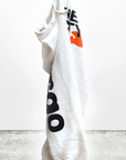 A white CIRCA'99 OG LETSGO OLDSCHOOL POLYBLEND/FLUFF sweat pant with black and orange lettering, hand-screen printed, hung on a hook against a plain, light grey background. The text on the hoodie is partially visible and stylized.