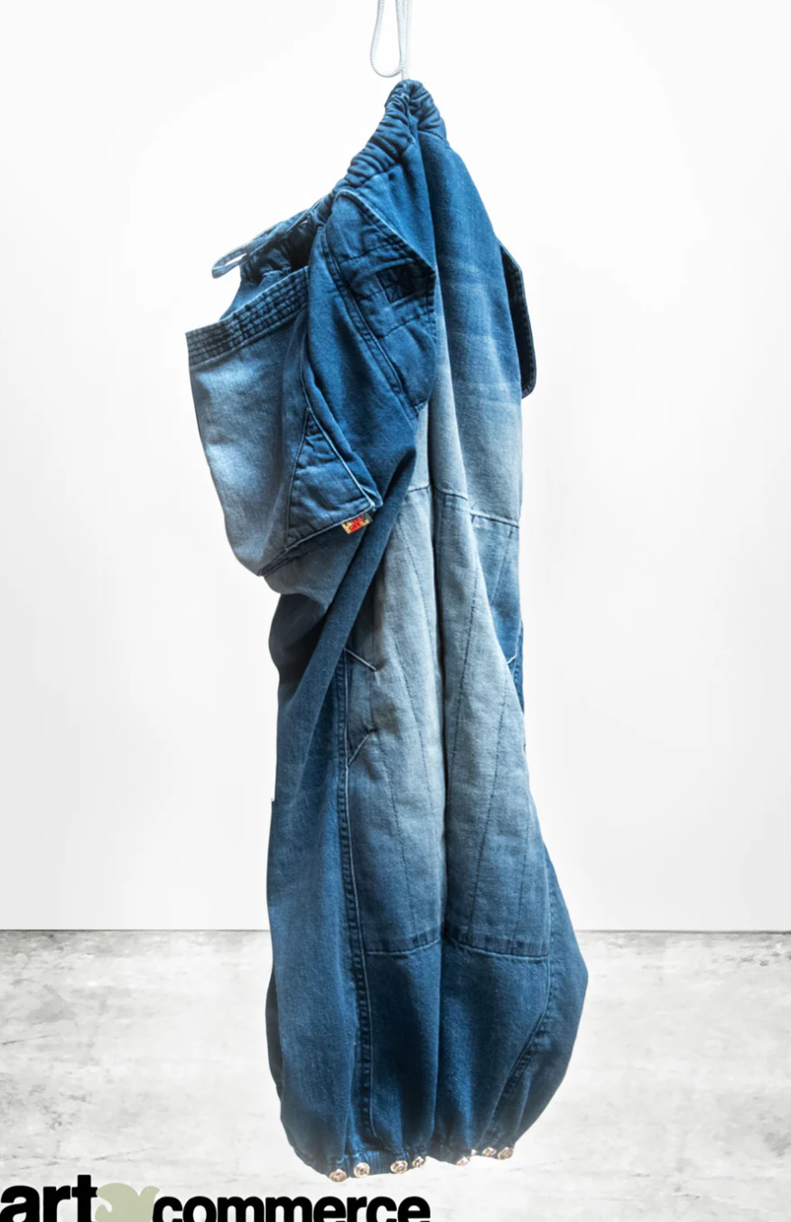 A pair of Free City FLAP/SNAP INDIGO pants hangs from a single white hanger against a plain white background, draped in such a way that one leg obscures much of the other.