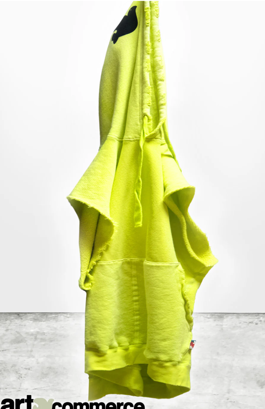 A bright yellow CUTOFF SUPERYUMM BIGGIE hoodie with a hood, shaped like a shark, hangs against a grey and white background. The hood features black shark eyes and a fin, crafted from lightweight French terry fabric.