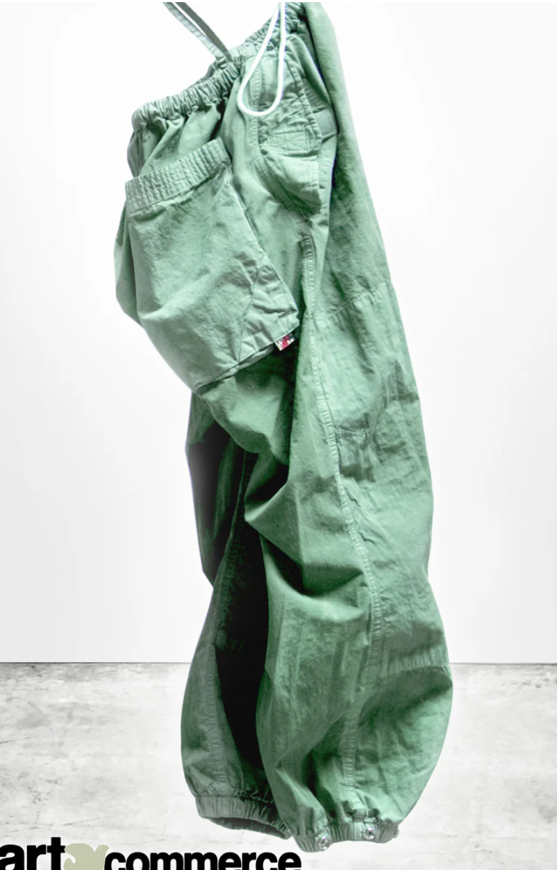 A pair of OUTOFSIGHT POPLIN/AIR FLAP/SNAP JUMPpants by Free City (sparrow, LLC), with drawstring waistband, hanging against a white concrete wall of a Scottsdale Arizona bungalow. The pants are wrinkled, giving a casual and used appearance.