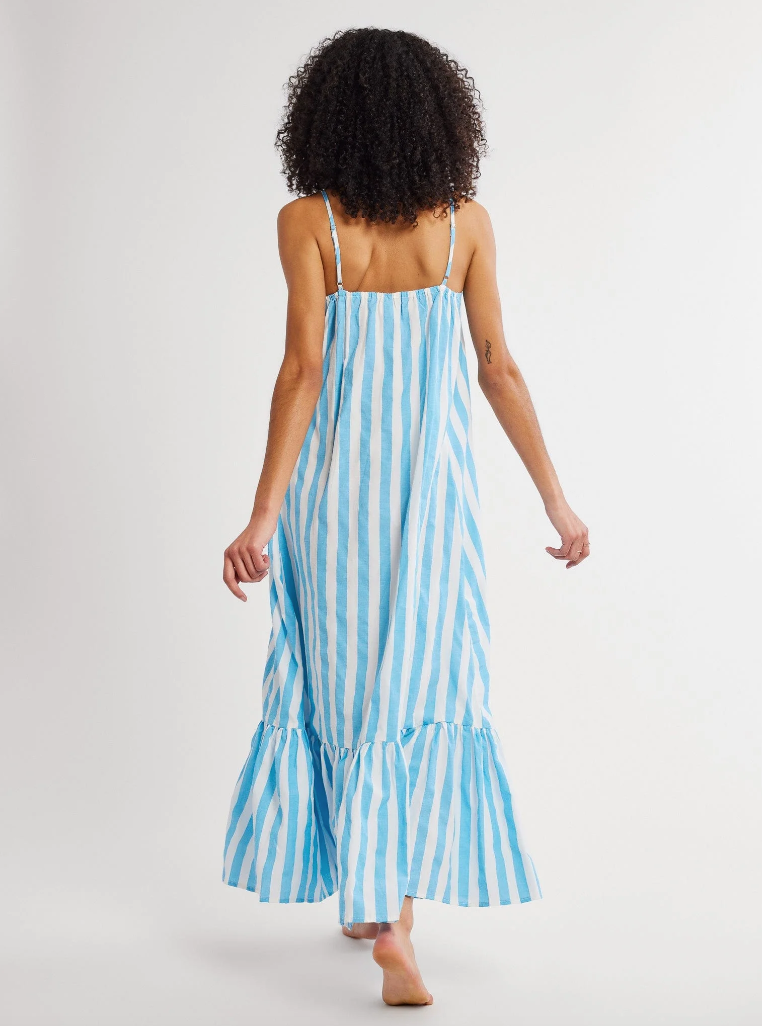 A woman with curly hair walking away from the camera, wearing a flowing blue and white striped Sienna Dress with spaghetti straps and a ruffled hem in Scottsdale, Arizona by Mille.