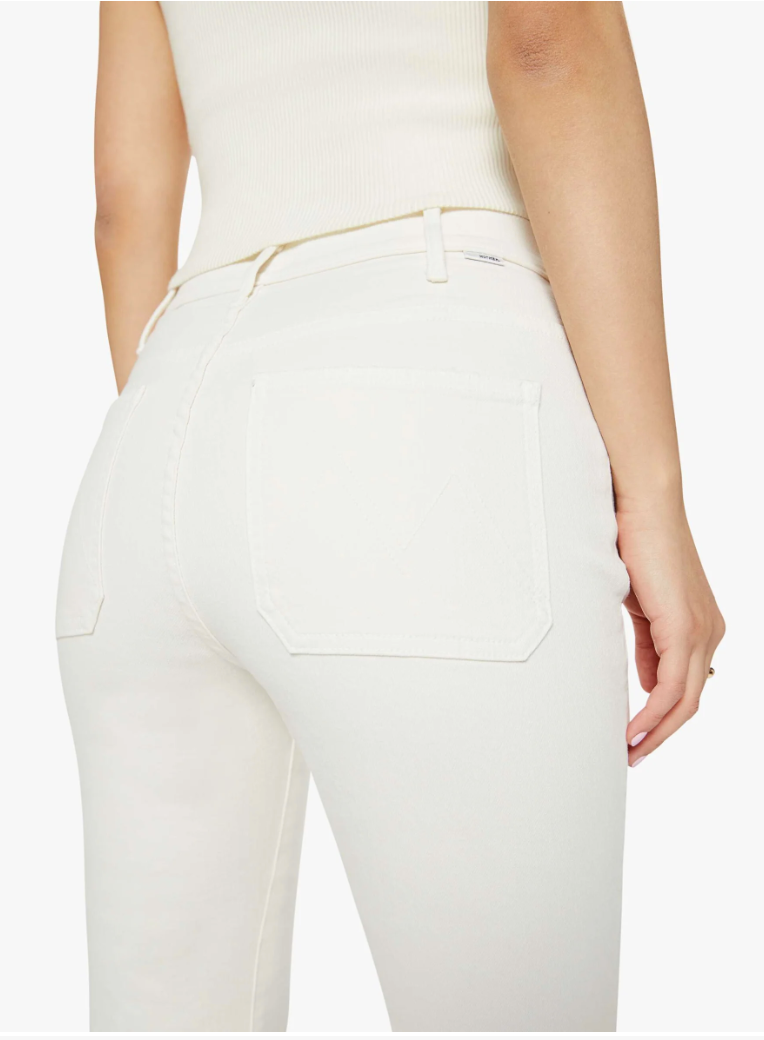 Close-up of a woman from behind wearing high-rise bootcut white jeans from Mother, focusing on the pocket detail with her hand resting lightly on her hip.