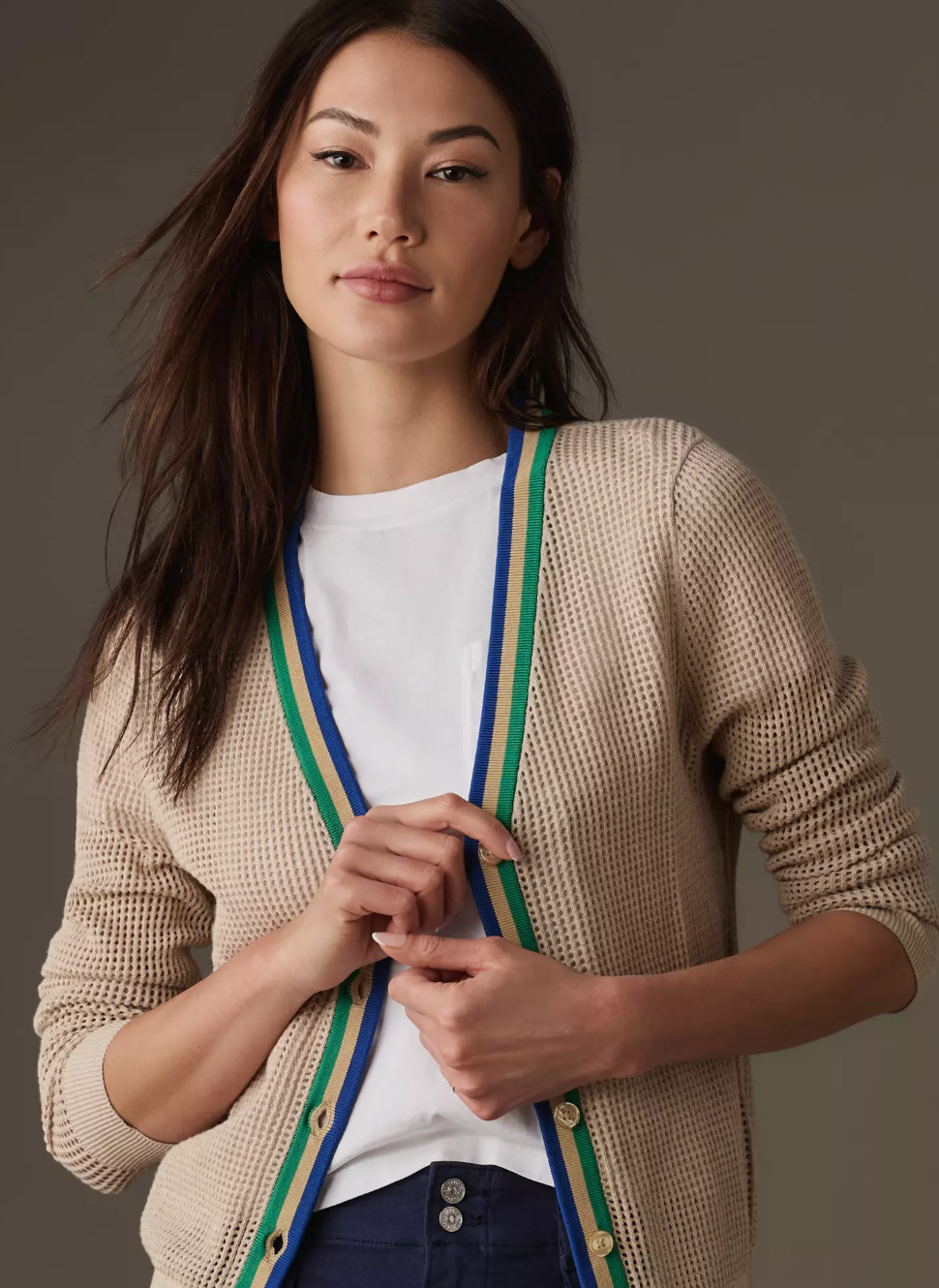 A woman with long dark hair wearing a Kule Zoey Cardigan with green and blue trim, layered over a white t-shirt, posing against a grey background in Scottsdale, Arizona.