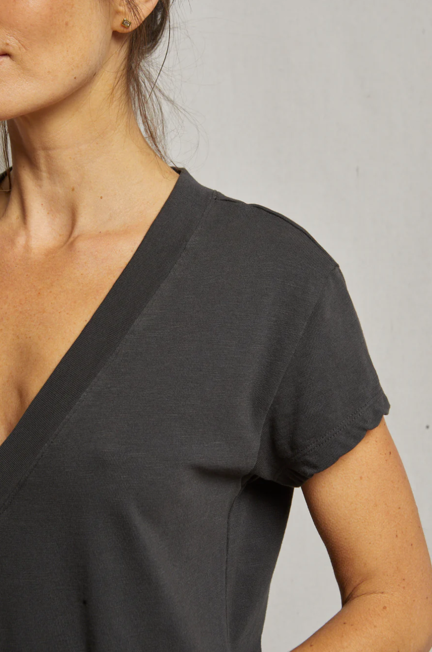 Close-up of a woman wearing a dark gray V-neck Perfectwhitetee T-shirt against a plain light background in a bungalow, focusing on the neckline and shoulder area.