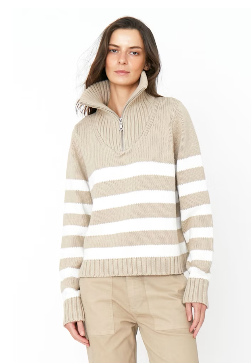A woman wearing a Kule striped, beige and white cotton quarter-zip sweater with a collar, paired with beige pants, standing against a plain white background.