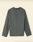 The Beautiful Mess Poet Blouse by Aquarius Cocktail is displayed against a cream-colored background. The minimalist design features a straight cut with long sleeves, and no visible buttons or pockets on the back. The fabric appears to be a smooth, medium-weight material with subtle hints of blue cotton chambray for added texture.