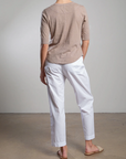 Rear view of a person on a concrete floor, wearing a beige 3/4 sleeve top, Pharaoh's Andy Pant with an elastic waist, and sandals, all against a plain gray wall in a minimalist setting.