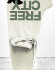 Beige FREECITY Large Sweatpants made from lightweight French terry are folded against a plain background. They feature "FREE CITY" in green, a black jumping animal silhouette, and have a visible white drawstring and part of the waistband. Brand: Free City (Sparrow, LLC).