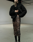 A person wearing the Le Superbe Liza Skirt, a black textured faux fur jacket, black lace-up boots, and a black headband stands in a minimalist industrial space.