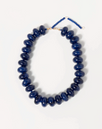 The Bailey Chunky Beaded Necklace by Faire features large, glossy dark blue marbled beads on a thin cord with an adjustable gold-tone clasp and beaded extension, shown against a plain white background.