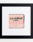 A framed print of a pink matchbook cover with the text "The Beverly Hills Hotel and Bungalows" in green cursive. The Match South Art Square Blk Frame with a white mat centers the matchbook cover, creating a minimalist and stylish display ideal for any modern decor.