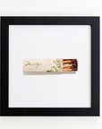 A Match South Art Square Blk Frame with a floral design and the word "Montage" on its cover is framed in a sleek black square frame. The box is slightly open, revealing some brown-tipped matches inside, and is centered within the white background of the frame, resembling an exquisite acrylic print.