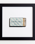 A framed print shows a matchbox with light blue and white diagonal stripes. The matchbox reads "The Darling Oyster Bar" and is displayed on a white background. The Match South Art Square Blk Frame surrounding the image contrasts beautifully, evoking an acrylic-like clarity that's both striking and elegant.