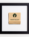 A Match South Art Square Blk Frame is displayed, featuring a beige cover with a green logo of a deer's head within a leaf shape, and the text "DEER VALLEY" beneath it. The black acrylic frame contrasts beautifully with the white background, creating a striking display that highlights every detail.
