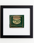 A framed green and beige matchbook from Houston's Restaurant is displayed against a white background. The matchbook features text reading "Houston's Restaurant" and "Restaurant and Cocktails" with an illustration of a restaurant facade in the center, all encased in a sleek Match South Art Square Blk Frame.