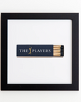 A framed black matchbox, known as the Art Square Blk Frame by Match South, displays "THE PLAYERS" text in white and a gold silhouette of a golfer. The matchbox, centered on a white background and encased in a sleek black acrylic frame, reveals several matches with black tips inside the open box.
