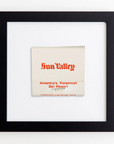 A framed matchbook with red text that reads "Sun Valley" at the top and "America's Foremost Ski Resort" below. The black frame features an acrylic finish, contrasting with the white background. The matchbook is centered within the frame. This is the Art Square Blk Frame by Match South.