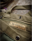 A close-up of the limited-edition Artist Tote by Made Worn shows a label reading "Handcrafted by MadeWorn, Los Angeles" stitched near the zippered pocket and metal snap button, emphasizing its craftsmanship.