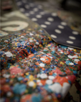 Close-up of colorful cotton canvas fabric with red, blue, orange, and white dots next to a Made Worn Artist Tote featuring a white polka dot pattern. The limited-edition tote appears slightly out of focus in the background.