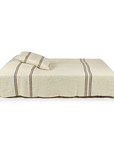 A neatly made bed features the Libeco Home Auburn Coverlet and matching pillow, both in cream with dark and light vertical stripes, against a plain white background.