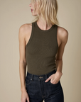 A woman with light blonde hair wears The Not So Basic Tank by Sold Out NYC and high-waisted dark jeans, standing against a beige background. She looks to her left with one hand in her pocket.
