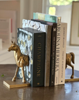 The Fox Run Brands Horse Bookend Set holds up several books, including "Champagne," on a table in a bright, window-lit room.