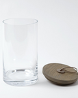 The Rustic Canister LG by Global Views is a clear, cylindrical glass jar with a round wooden lid and leather loop—perfect as a food-safe container for modern or rustic kitchen storage.