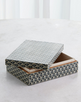 The Interwoven Box MD by Global Views is a decorative resin storage box featuring a blue and cream geometric pattern, pictured with its lid partially open on a light-colored surface.