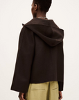 A person with short hair is shown from behind wearing the BA&SH Jacket Kove, a dark brown, loose-fitting style with a wide collar, paired with light green pants against a plain, light background.
