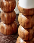 Close-up of two hand-crafted Pillar Candleholders by Two's Company, featuring smooth, rounded shapes and topped with white candles, set on a dark wooden surface for a mid-century modern look.