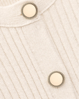 Close-up of the BA&SH Dress Anisa's cream-colored ribbed knit wool blend fabric, detailed with two round ivory buttons featuring decorative metallic edges.