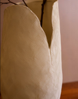 The Bloom Flower Vase L by Kalalou, Inc features a textured cream finish and uneven rim, holding bare branches on a wooden surface against a light, plain background.