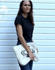 A woman in a black t-shirt and blue jeans stands before a white wooden wall, holding the Kempton & Co. Oversized Clutch featuring a black spider design.