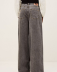 Someone models the BA&SH Jean Yusc—loose-fitting, wide-leg gray 100% cotton jeans with large back pockets—paired with a black and white long-sleeve top, shown from behind on a plain background.