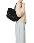 A person in a beige sweater and light blue jeans carries the Jerome Dreyfuss Leon S handbag, an organized leather bag adorned with silver grommets. The image is cropped to show only the upper body and the bag.