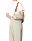 A person is seen from the back wearing a white t-shirt, high-waisted beige pants featuring the Gaucho Ceinture/Belt by Jerome Dreyfuss, and carrying a light beige crossbody bag with a wide brown strap.