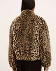 A person with long dark hair, seen from behind, wears the BA&SH Coat Jaros Leopard faux fur jacket and black pinstripe pants against a plain light background.
