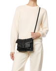 A person in a cream sweater and pants carries the Jerome Dreyfuss Harry Handbag—a black goatskin crossbody with a front flap and buckle detail. The image is cropped at the neck.