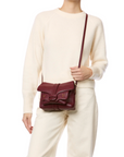 A person in an ivory sweater and matching pants holds the Jerome Dreyfuss Harry Handbag, a maroon goatskin crossbody with a flap closure and gold accents. The image is cropped at the shoulders and mid-thigh.
