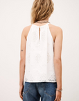 A person with wavy, blonde hair is seen from behind wearing the BA&SH Top Maxi, a sleeveless broderie anglaise cami top with a back keyhole, styled with blue jeans against a plain background.