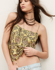 A woman in the BA&SH Top Pamela, a yellow patterned cropped top with metallic bead details, pairs it with light-wash jeans. She has loose long brown hair and accessorizes with layered necklaces and rings against a neutral background.