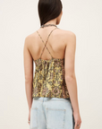 A woman with long dark hair models the BA&SH Top Pamela—a yellow and brown patterned halter crop top with metallic bead details and open back—paired with light blue high-waisted jeans, facing away from the camera against a plain background.