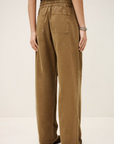 A person models the BA&SH Pant Fima—loose-fitting, high-waisted brown cotton linen pants with an elasticated waist and back pockets—against a neutral background, showing only the lower half of the body.